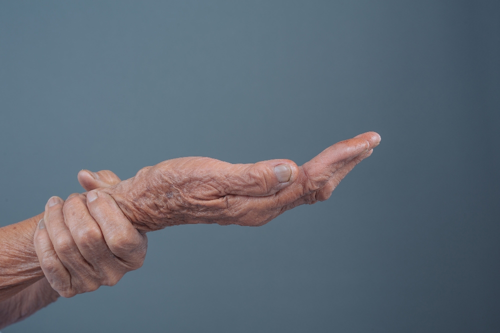 Elderly hand gently bent back against gray backdrop.